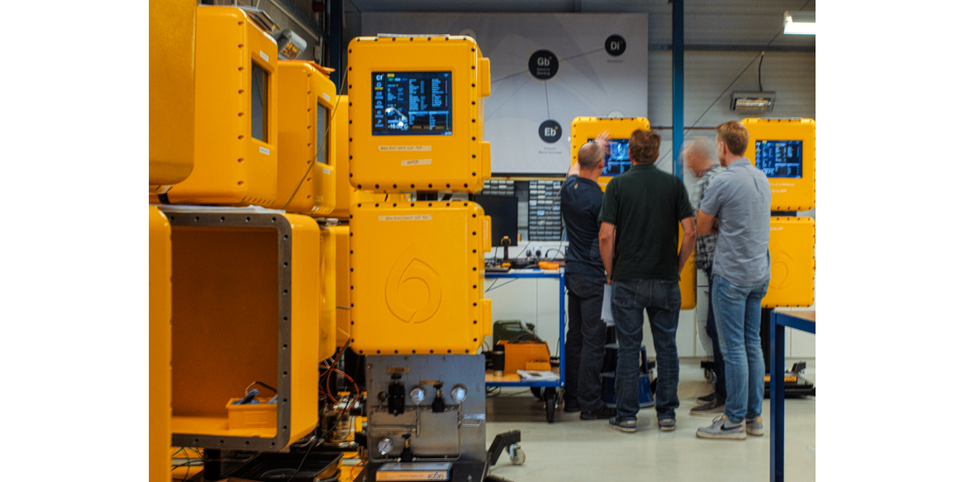 The image focuses on Icon's distinctive yellow analysers - there are four in the foreground of the picture, and two further back. Four people are stood around one of the analysers at the back of the image, being shown a graph on the analyser display.